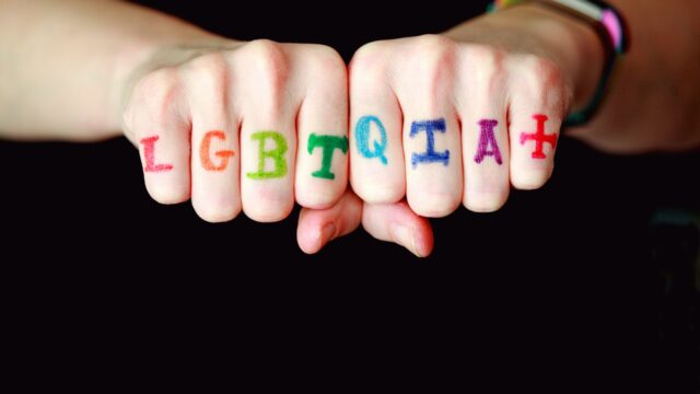 lgtqia+ writting on the knuckles of two hands in rainbow colors